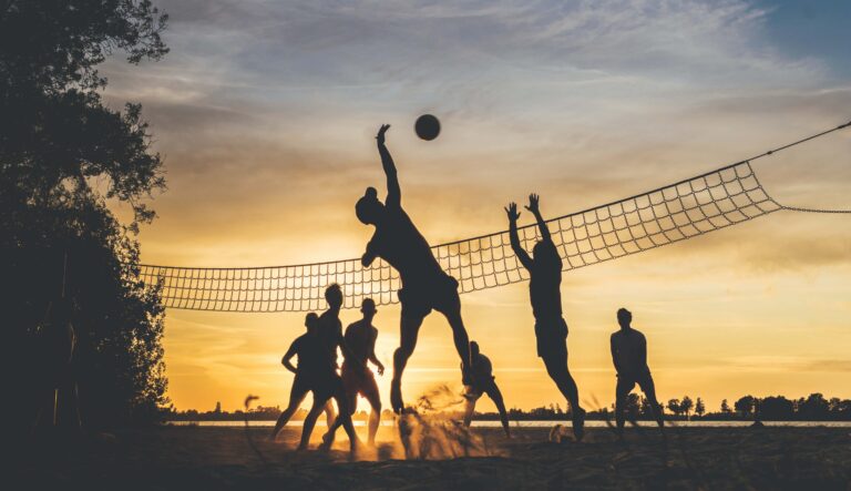 Auf dem Bild spielen Menschen Volleyball im Sommer. Der Sport im Sonnenuntergang steht für den positiven Zusammenhang von Sport und Psyche